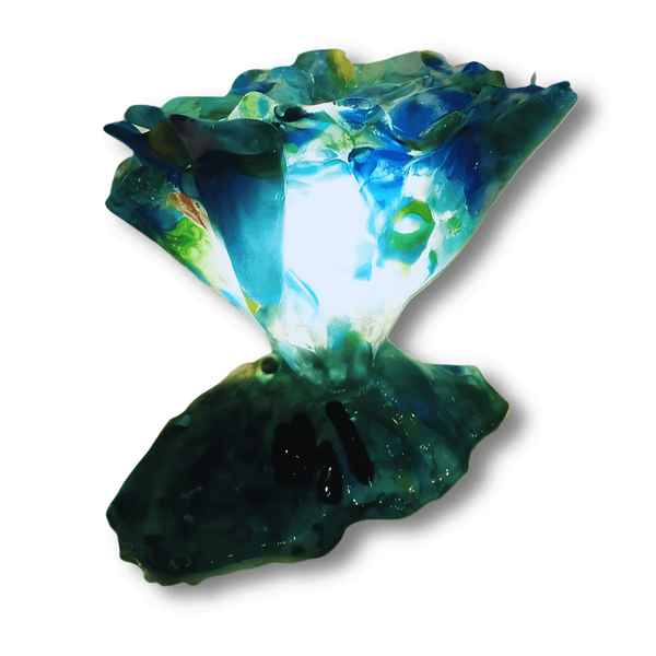 A unique, handcrafted fused glass lamp featuring vibrant shades of blue, green, and white. The lamp has an abstract, sculptural shape with a flowing glass design that emits a soft, colourful glow